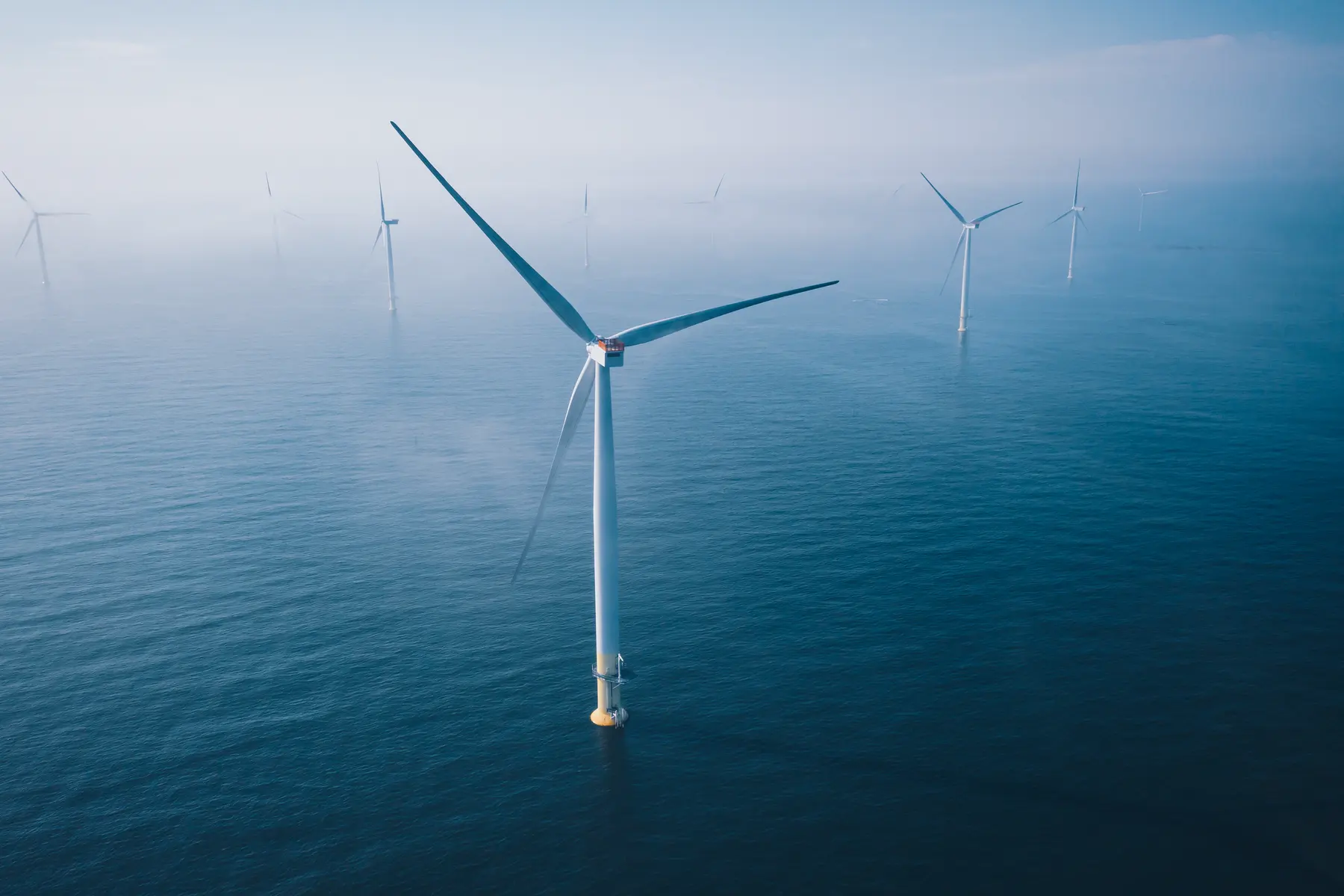 Wind turbines standing in a calm sea under a hazy sky