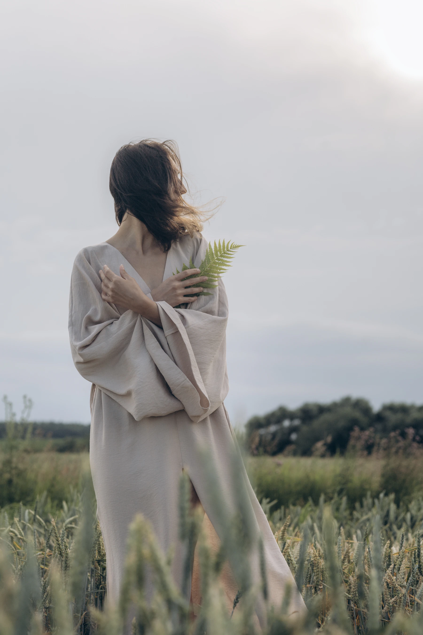 Woman in an oat linen dress holding a fern in a field