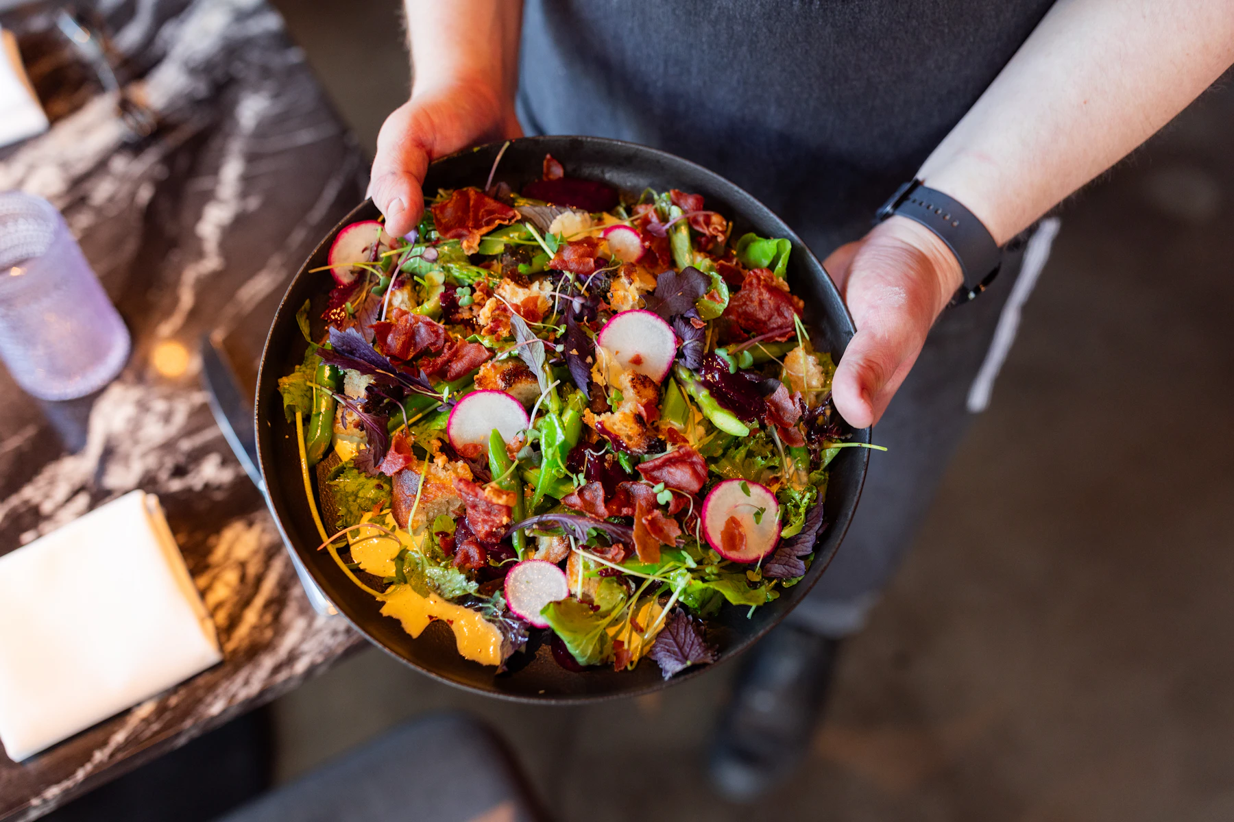 Hands holding a bowl of greens, radish and roasted vegetables