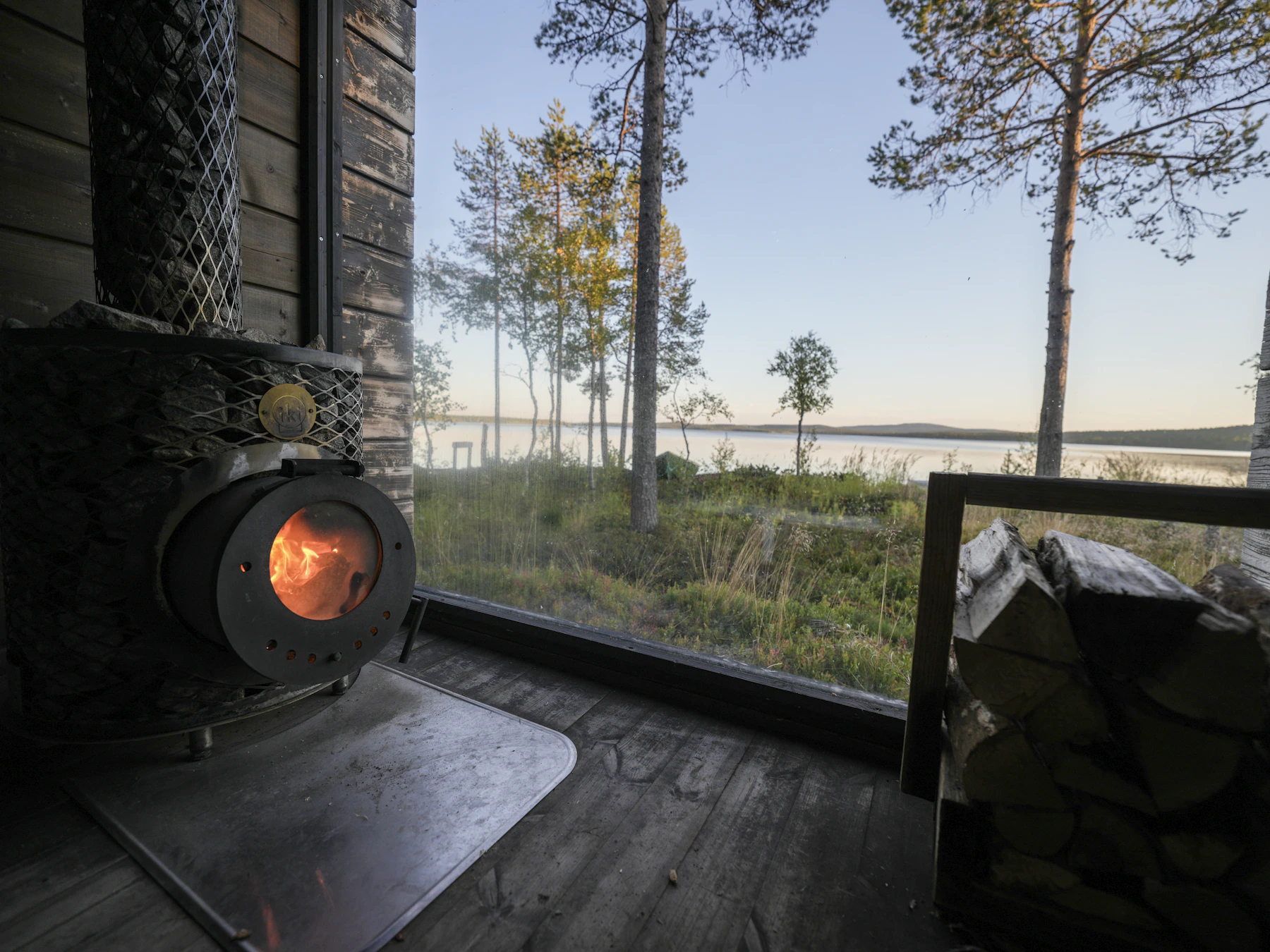 Cabin interior with a wood stove and a wide window onto a lake