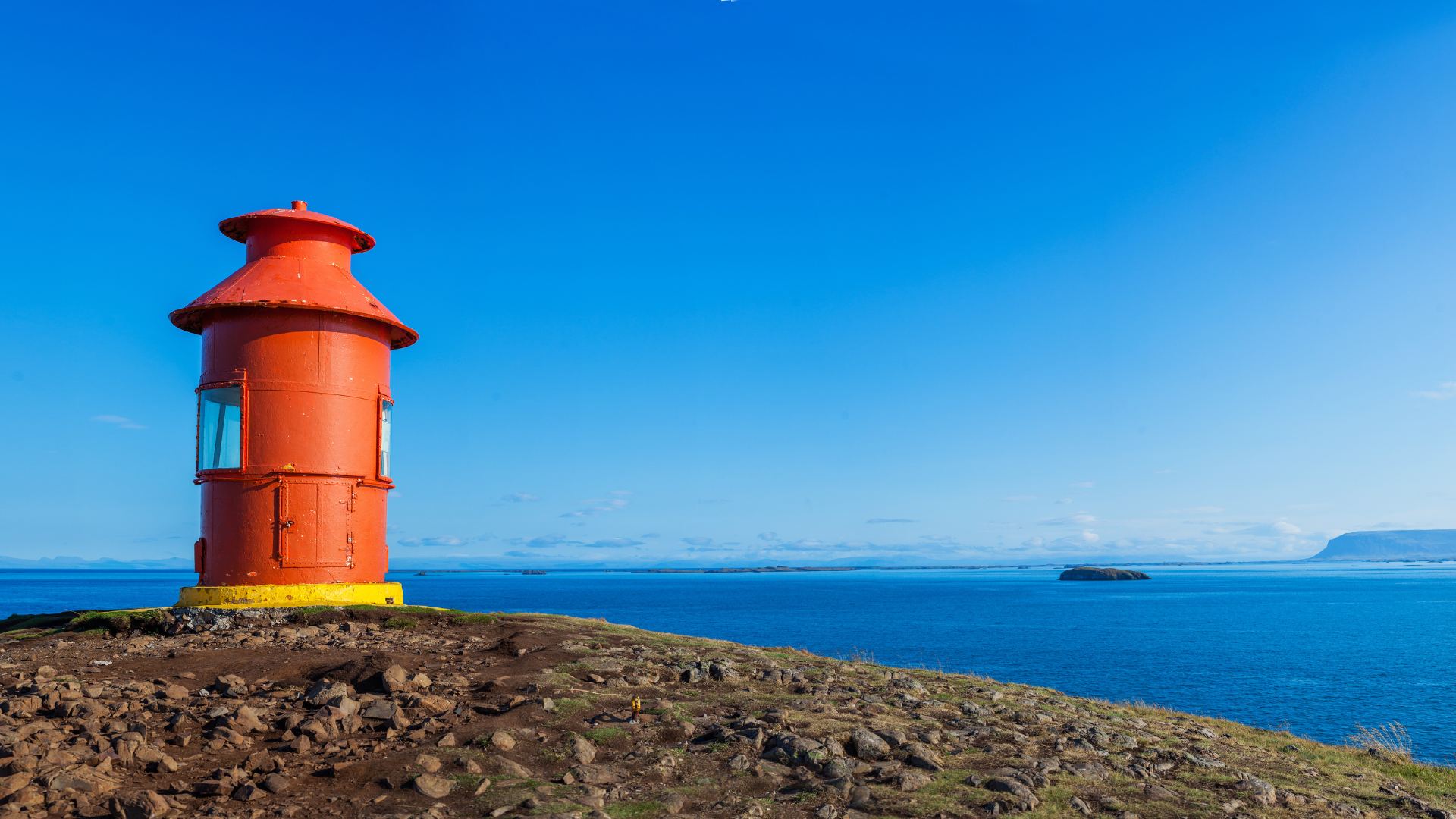 Red lighthouse on a rocky coast under a clear sky