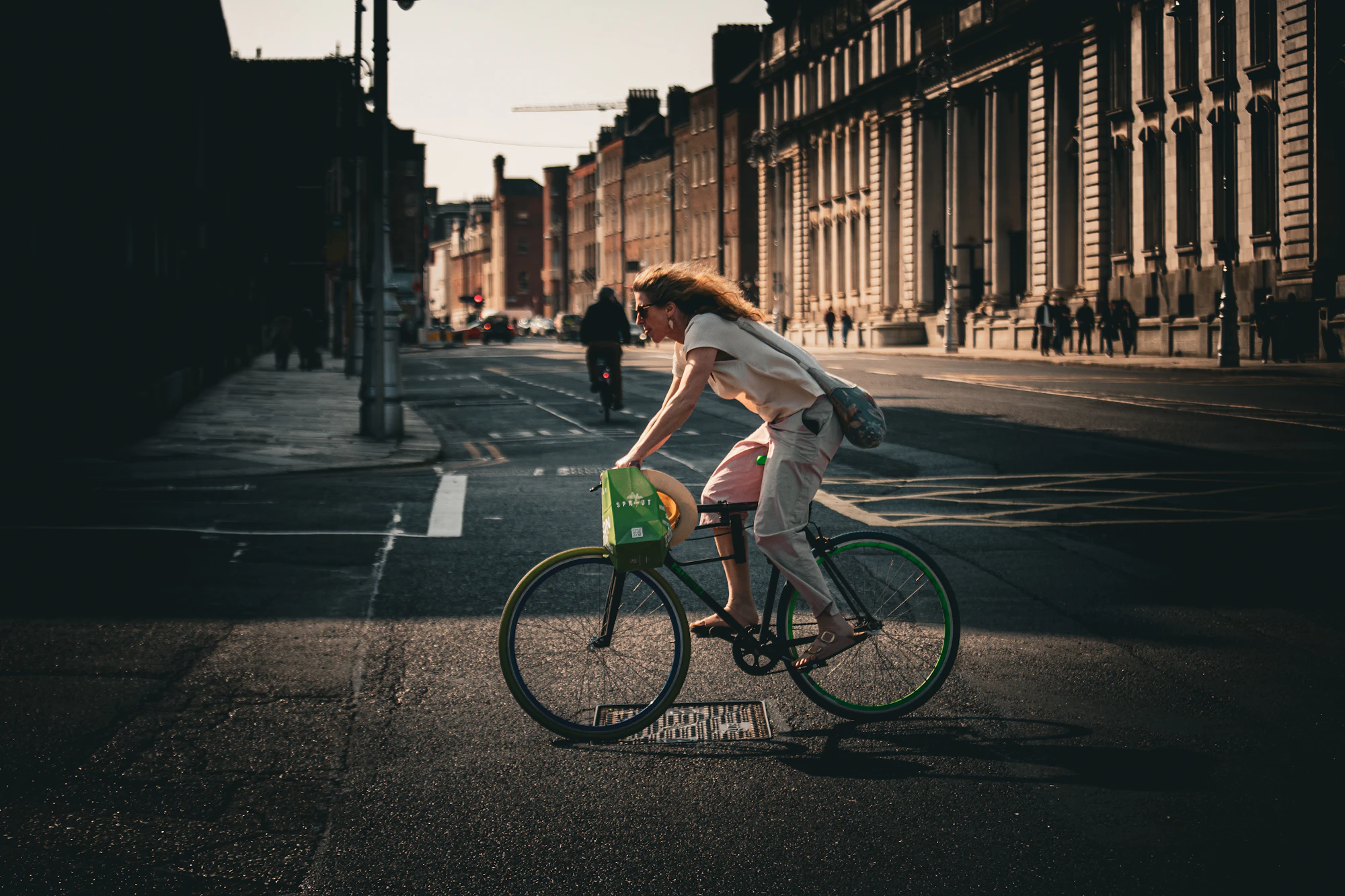 A woman rides a bicycle down an empty city street in the last light of the day