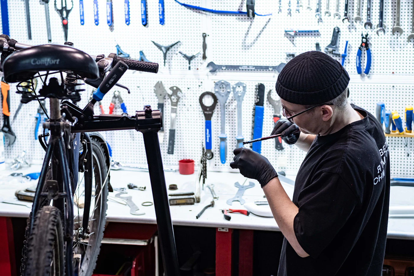 A mechanic works at a bench in front of a wall of tools