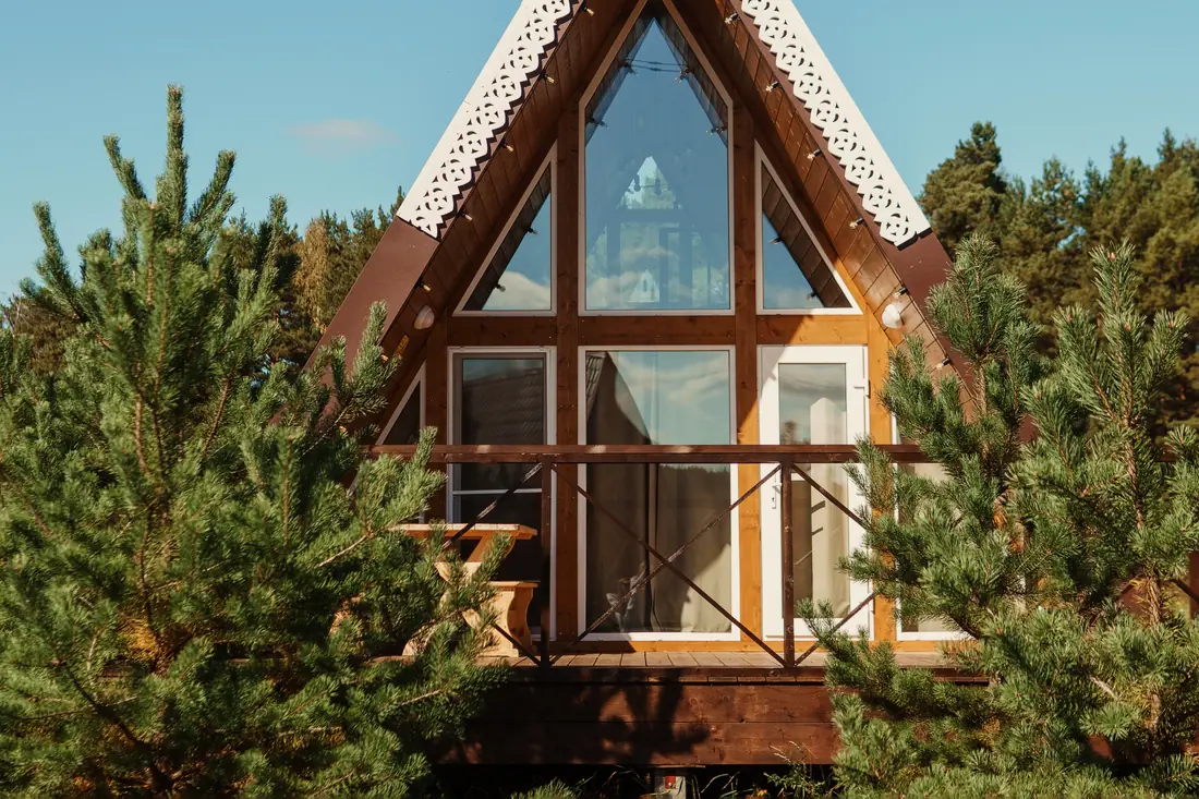 A wooden A-frame cabin with a tall glass front among pine trees