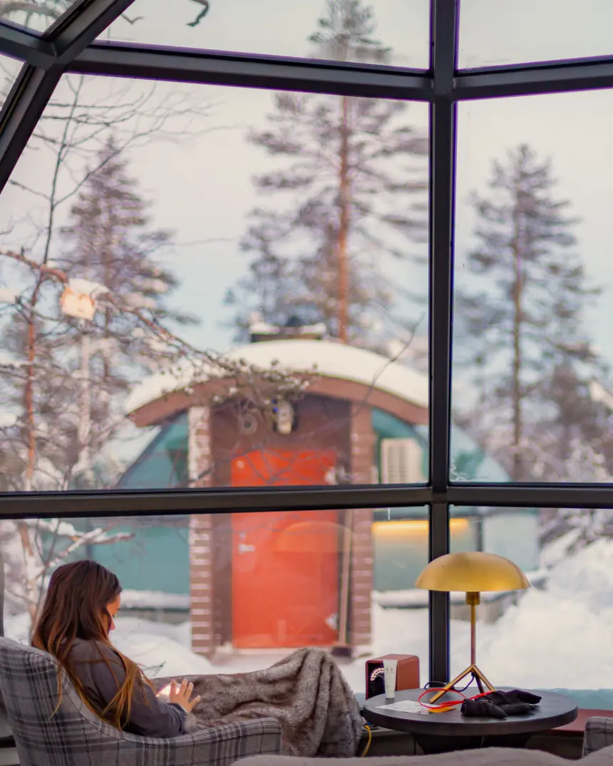 A woman under a blanket by a glass wall, with snow outside