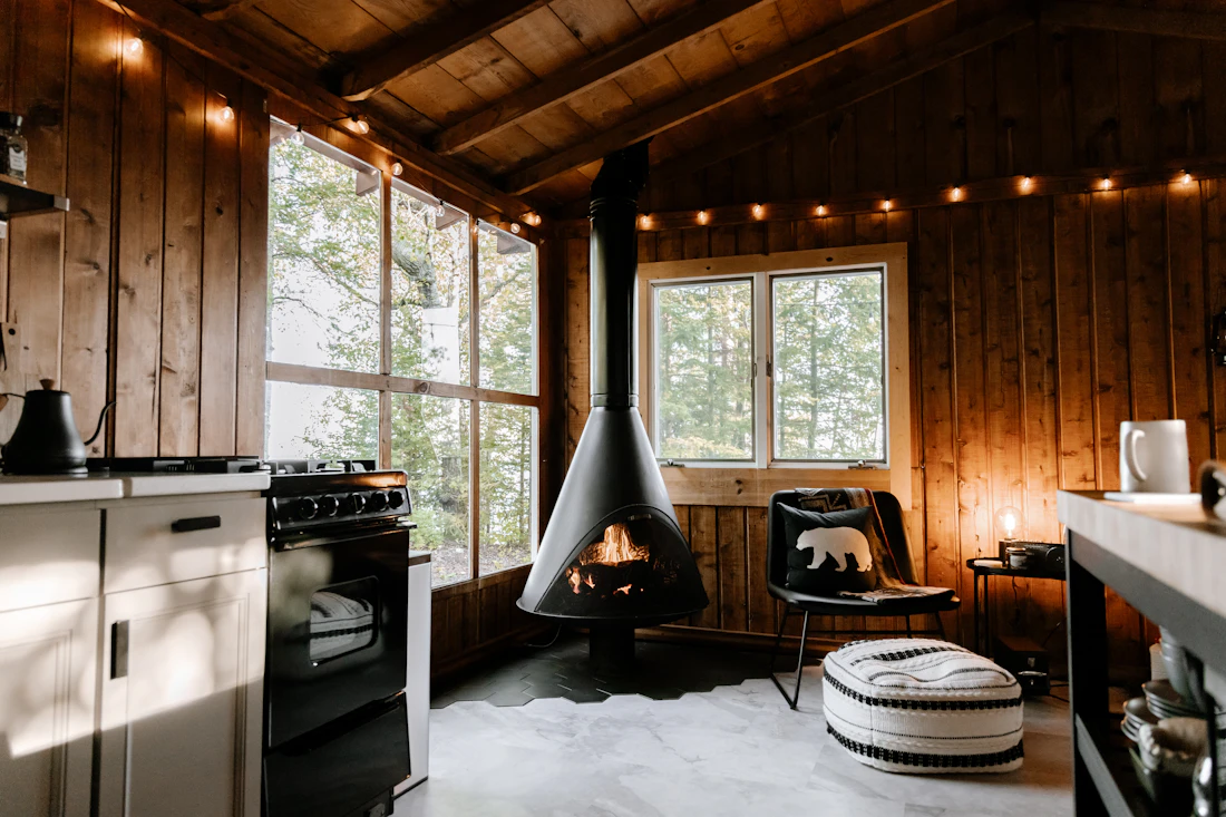 The inside of a wooden cabin with a hanging stove and warm string lights