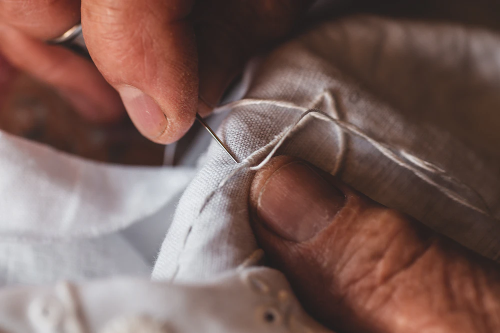 Hands stitching fabric by needle and thread